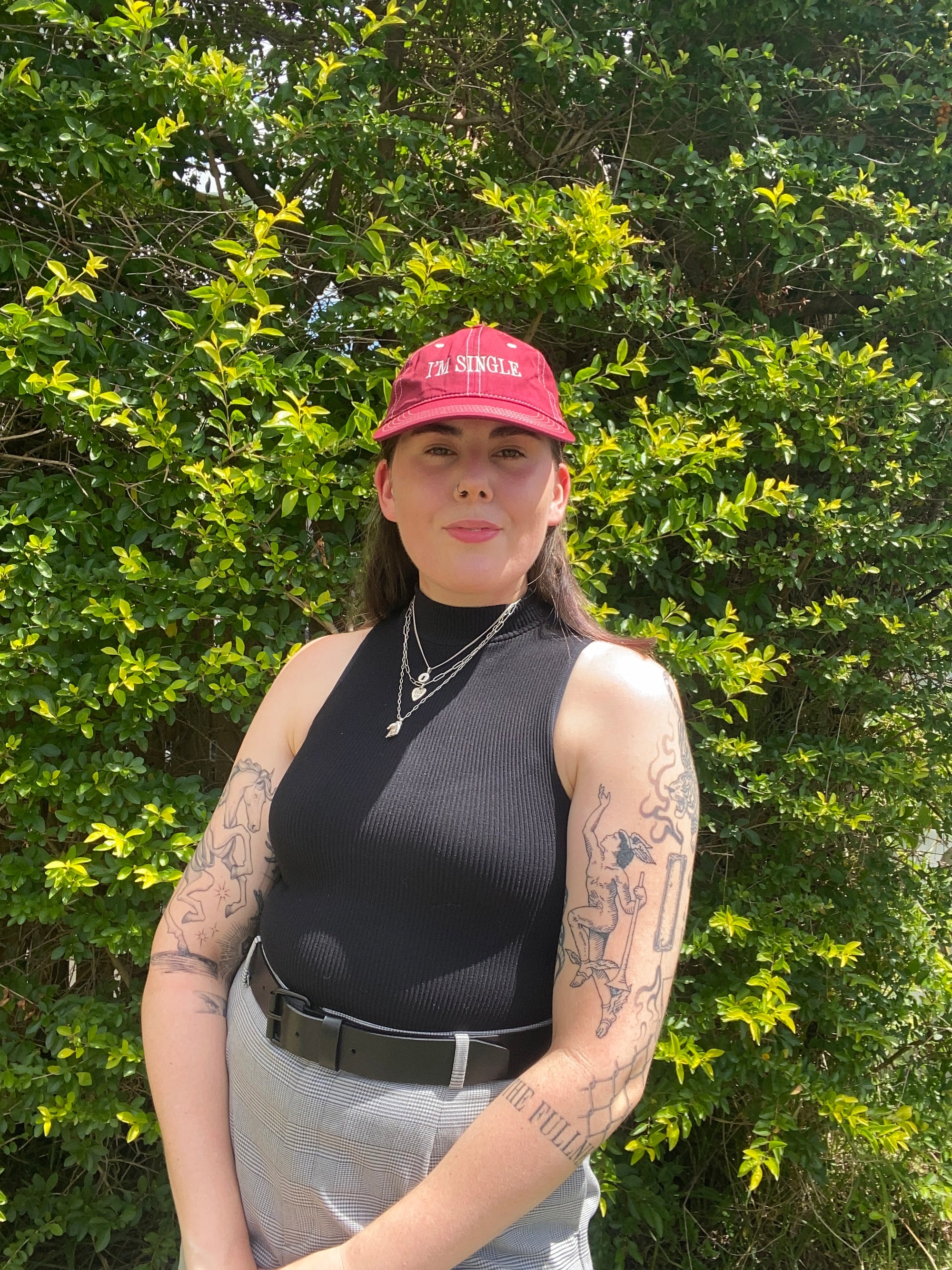 Person wearing a black sleeveless top and pink cap standing in front of green foliage