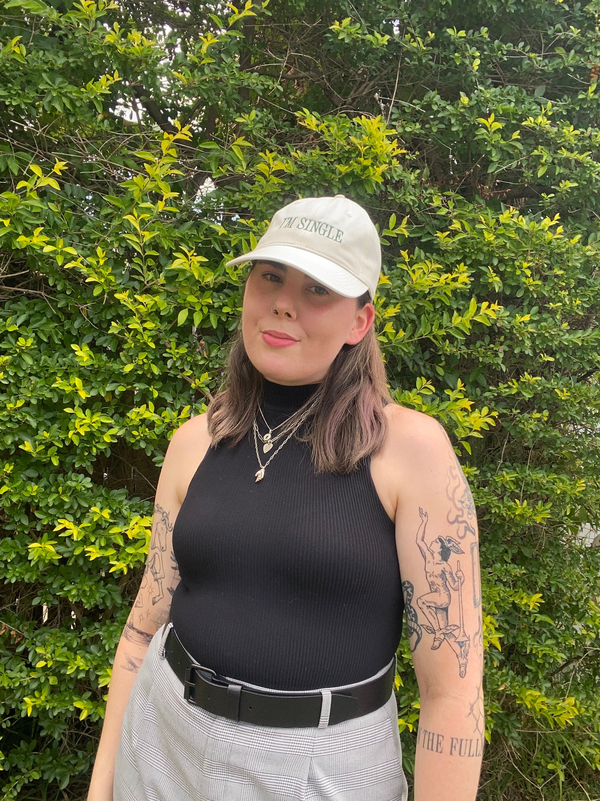 Person wearing a black tank top and white cap outdoors with greenery in the background