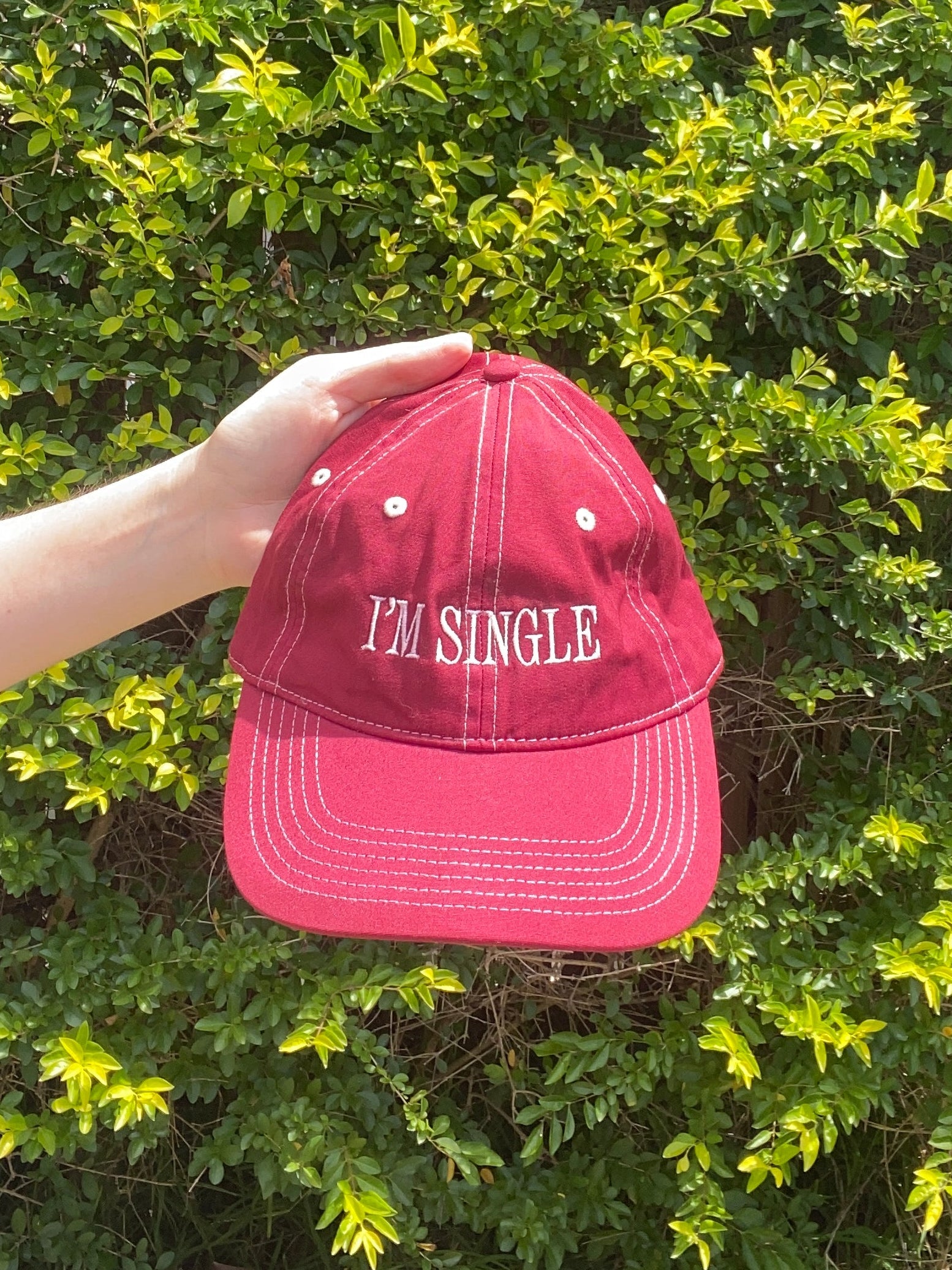 shiraz cap with text that says "i'm single" held up against a green bush